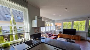 Eine moderne Küche mit einem großen Fenster, einem Einbauofen und einem Essbereich mit einem roten Sofa und einem Fernseher.
