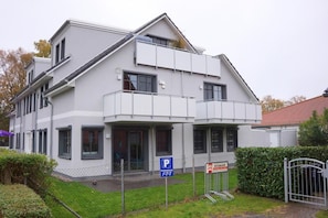 Un bâtiment à deux étages, doté d’un toit plat, d’un balcon au deuxième étage et d’un panneau indiquant la présence d’un parking.