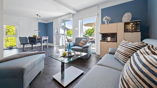 En moderne stue med et glasbord, grå sofaer og et spiseområde med stole og bord.