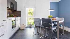 Et moderne køkken med indbyggede apparater, et spiseområde med bord og stole, samt et vindue med udsigt til grønne omgivelser.