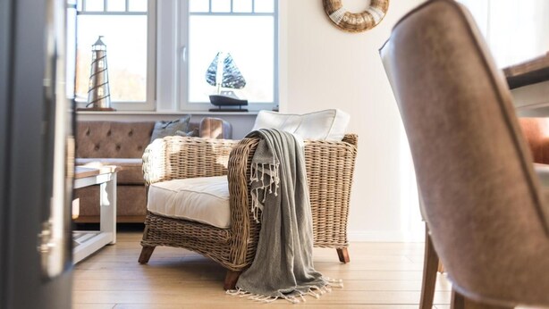 A cozy living room with a wicker sofa, a grey throw blanket, and a wicker chair.