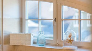A window with a view of buildings, a glass vase, and a decorative item on a ledge.