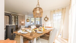 A dining area with a wooden table set for breakfast, a black wood stove, and a wicker chandelier.
