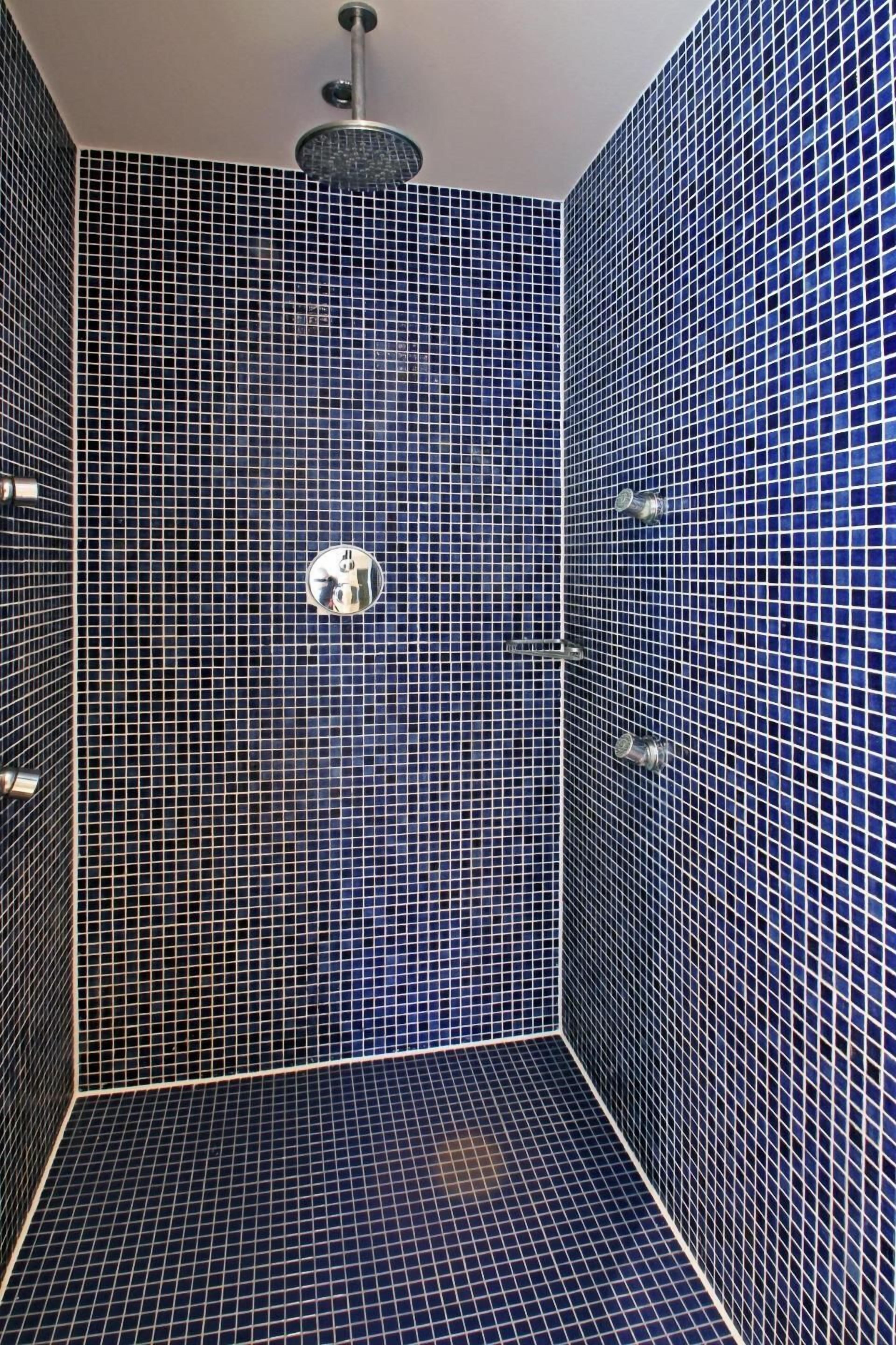 A bathroom with a tiled floor and walls, a showerhead, and a mirror.
