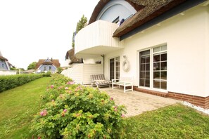 A house with a curved roof, a balcony, and a garden with pink flowers.