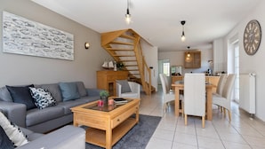 Een moderne woonkamer met een grijze bank, een houten salontafel en een trap naar een verdieping erboven.