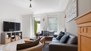 Een moderne woonkamer met een grote flatscreen-tv, een houten kast, een leren bank en een eethoek.
