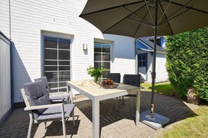 Eine Terrasse mit Tisch, Stühlen und einem großen Sonnenschirm, begrenzt durch eine Hecke.