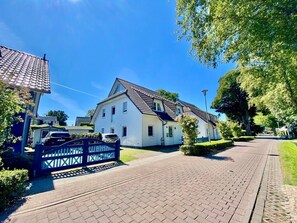 Eine Wohnstraße mit einem weißen Haus, einer gepflasterten Straße und einem blauen Tor.