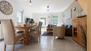 Een ruime woonkamer met een eettafel, stoelen, een bank en een open haard.