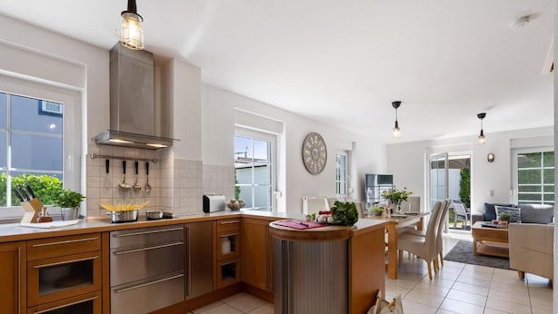 Een moderne keuken met houten kastjes, roestvrijstalen apparatuur en een centraal eiland. Er is een eethoek met een tafel en stoelen, en een zithoek met een bank en salontafel.
