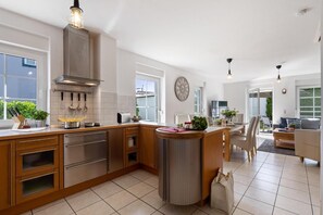 A modern kitchen with wooden cabinets, stainless steel appliances, and a central island. There is a dining area with a table and chairs, and a living room with a sofa and a coffee table. - Alte Reihe 14 "Haus Teja" (incl. Sky) - semi-detached house including Netflix and (Zingst)