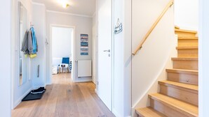 Un corridoio con una scala in legno, una porta con un cartello e una sedia blu sullo sfondo.