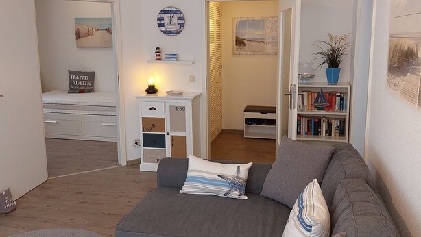 Een gezellige woonkamer met een grijze bank, een klein wit kastje en een boekenkast.