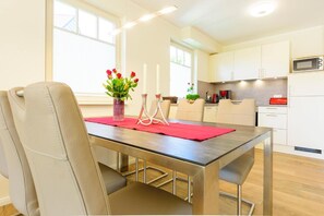 A modern kitchen with white cabinets, a microwave, and a dining area with a table set for two. - Kavelweg 15a "Heimathafen" - comfortable townhouse (Zingst)