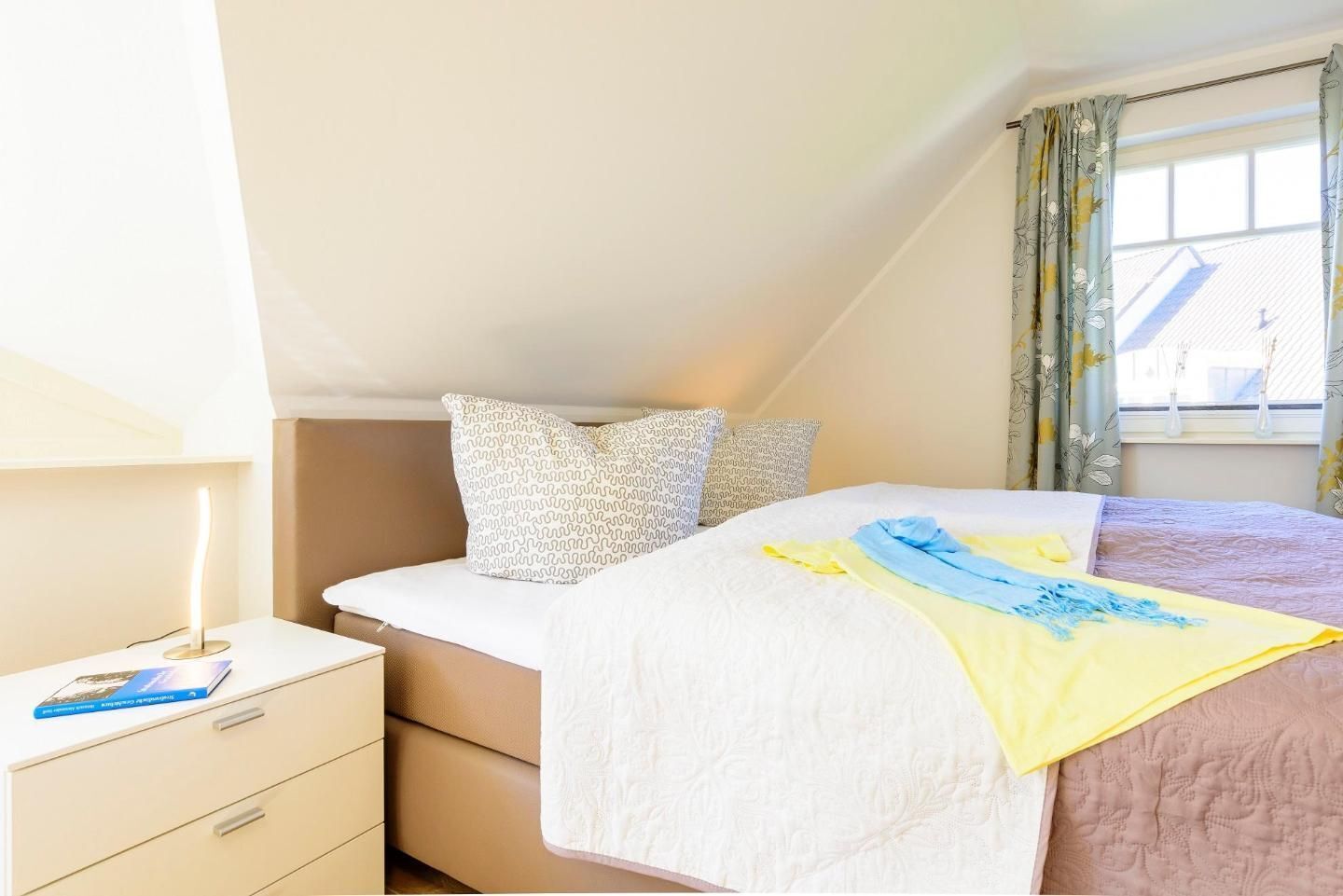 A bedroom with a bed, a bedside table with a lamp, and a window with curtains.