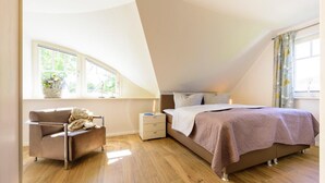 Un dormitorio con cama, una silla, mesita de noche y ventana con vista a vegetación.