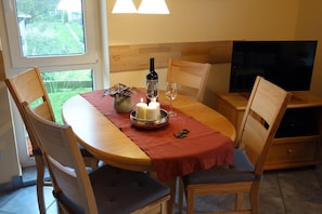 Mesa de jantar oval com toalha vermelha, rodeada por cadeiras de madeira com assentos acolchoados.