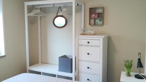 Een slaapkamer met een bed, een kledingkast, een dressoir en een klein tafeltje met een lamp.