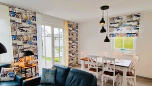 Ein Wohnzimmer mit schwarzem Ledersofa, einem Esstisch mit weißen Stühlen und einer Wand mit Muster.