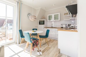 Una cocina moderna con armarios blancos, encimera de madera y comedor con una mesa redonda y sillas azules.