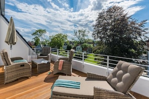 Un balcón con mobiliario de mimbre, una mesa y vistas del barrio circundante.