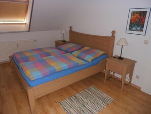 A bedroom with a wooden bed, two bedside tables, a floor lamp, a radiator, and a framed picture on the wall.