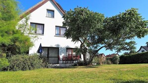 Une maison à deux étages, avec une façade blanche, un toit rouge et un arbre dans le jardin.