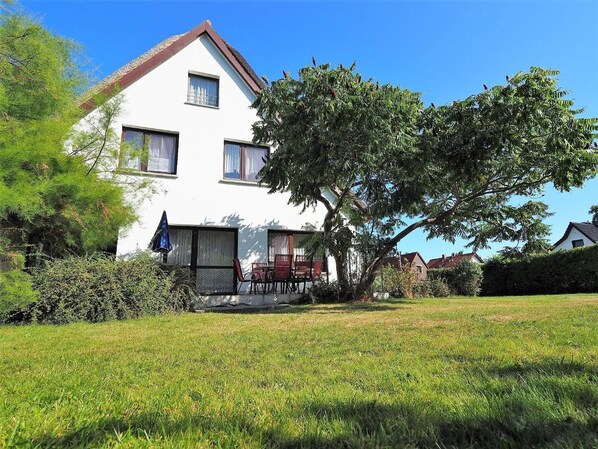 Une maison à deux étages, avec une façade blanche, un toit rouge et un arbre dans le jardin.