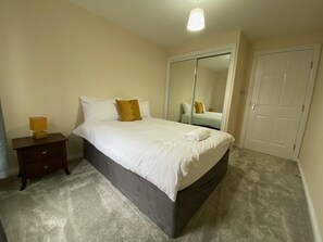 A bedroom with a bed, a nightstand, a mirror, and a door.