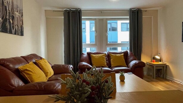 Ein Wohnzimmer mit einem braunen Ledersofa, zwei gelben Kissen, einem Holztisch und einer kleinen Topfpflanze.