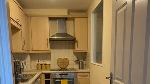 Eine kleine Küche mit Holzschränken, einer Edelstahl-Dunstabzugshaube, einer Waschmaschine und einem Mülleimer.