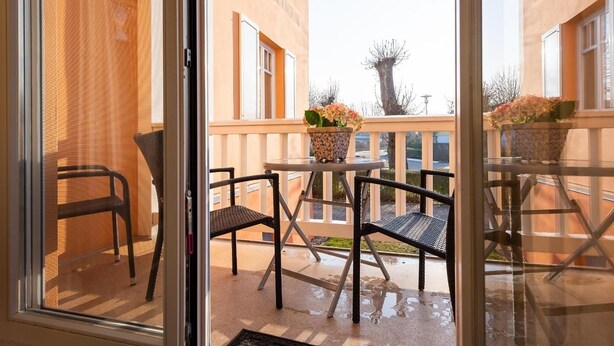 A balcony with two chairs and a table, a potted plant, and a view of a building with a tree. - Neue Reihe 22 Whg. 1 "Villa Balticum" - Modern vacation apartment close to the center (Zingst)
