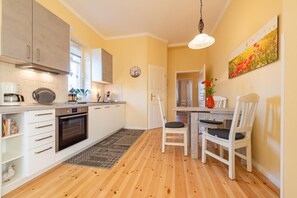 A modern kitchen with white cabinets, a built-in oven, and a dining area with a table and chairs.