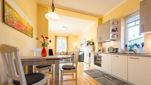 A modern kitchen with white cabinets, a dining area with wooden chairs, and a large window providing natural light. - Neue Reihe 22 Whg. 1 "Villa Balticum" - Modern vacation apartment close to the center (Zingst)