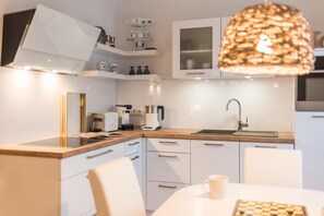 Una cocina moderna con armarios blancos, horno empotrado, cafetera y una lámpara colgante.