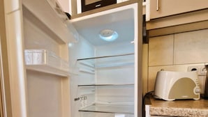 An open refrigerator with clear shelves, a microwave above, and a toaster on the counter.