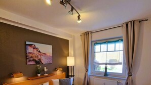 A double bed with white bedding, a bedside table with a lamp, a wall-mounted picture, and a window with curtains.