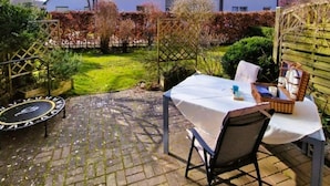 A patio with a table and chairs, a trampoline, and a house in the background.