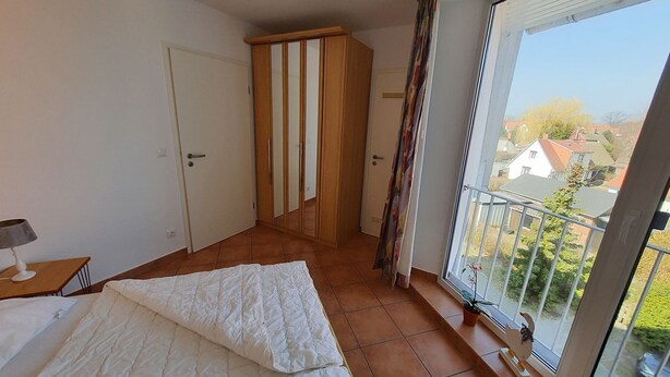 Et soveværelse med seng, skab, dør og en balkon med udsigt til huse.