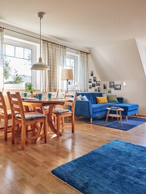 Una sala de estar moderna con comedor, un sofá azul, muebles de madera y un amplio ventanal con cortinas.