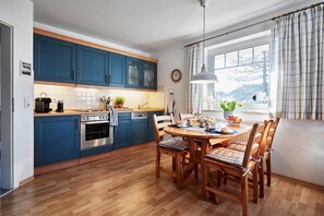 Une cuisine moderne avec des meubles bleus, une table à manger en bois et une vue sur l’extérieur par une fenêtre.