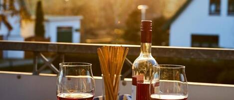 A table with two wine glasses, a bottle, and a plate of olives on a balcony with a sunset view.