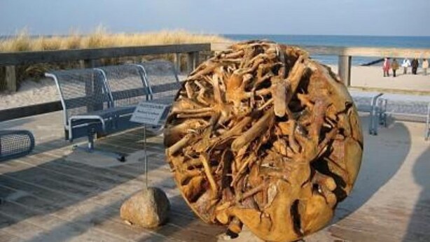 Una gran escultura de madera en un paseo marítimo cerca de la playa.