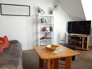 Un salon comprenant un canapé, une table en bois, une bibliothèque, un téléviseur et un ventilateur de plafond.