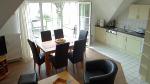 Cocina compacta con comedor, que incluye una mesa con sillas, una pequeña zona de café y vistas a través de la puerta de cristal.