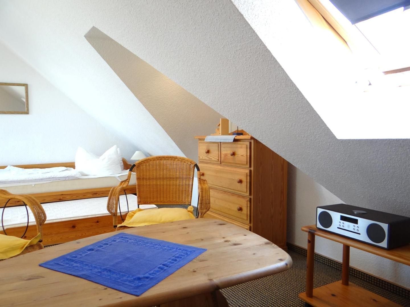 A bedroom with a sloped ceiling, a bed, a chair, a dresser, and a radio on a small table.