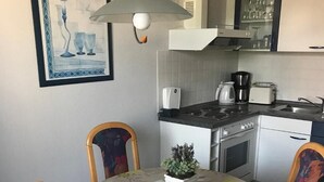 En spiseplads med et rundt bord, fire stole, en potteplante og et køkken i baggrunden.