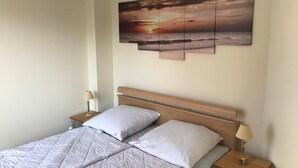 Et hotelværelse med en seng, to sengeborde og et kunstværk på væggen, der viser en solnedgang over havet.