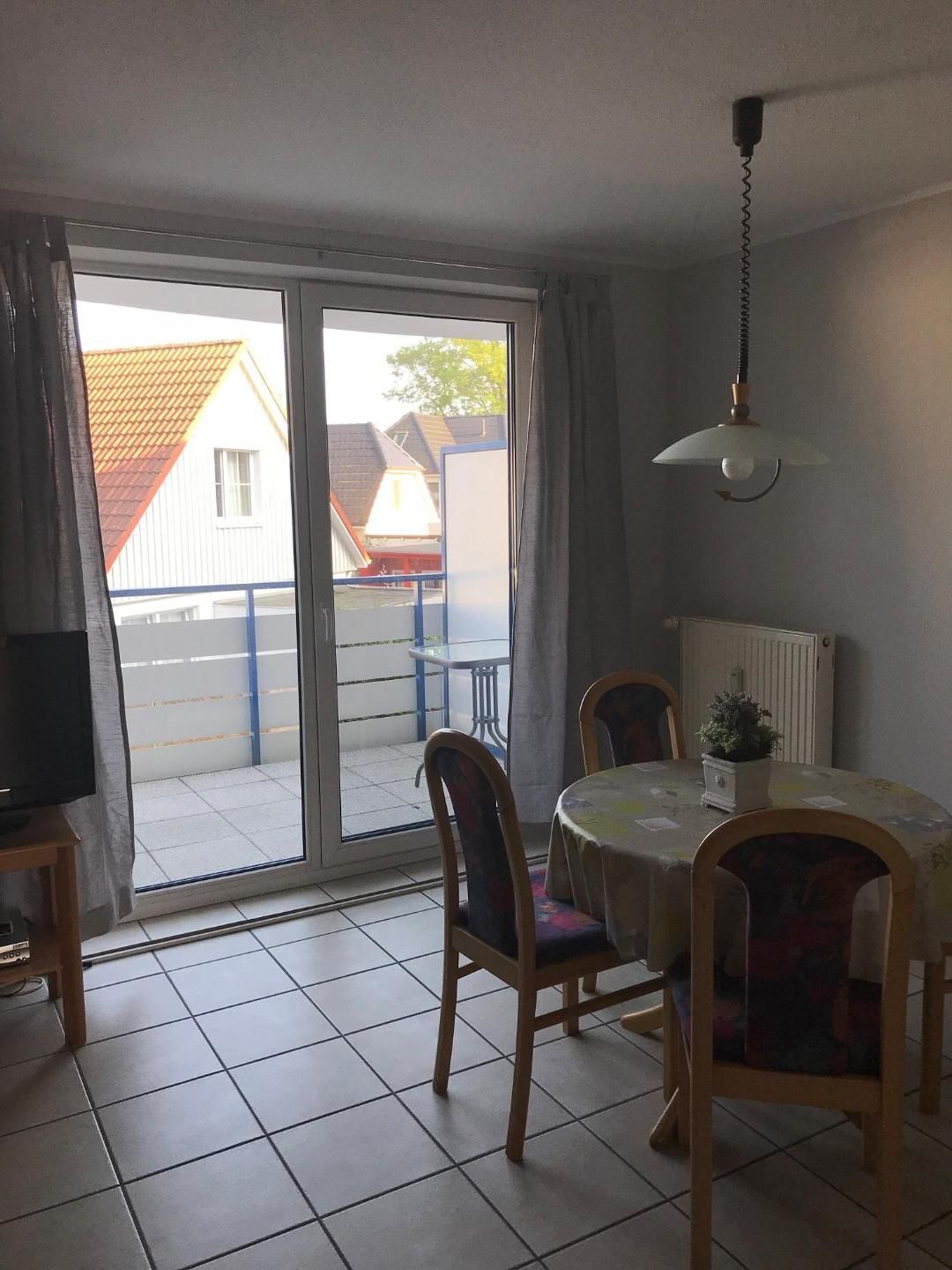 A room with a dining table, chairs, a TV, and a sliding glass door leading to a balcony.